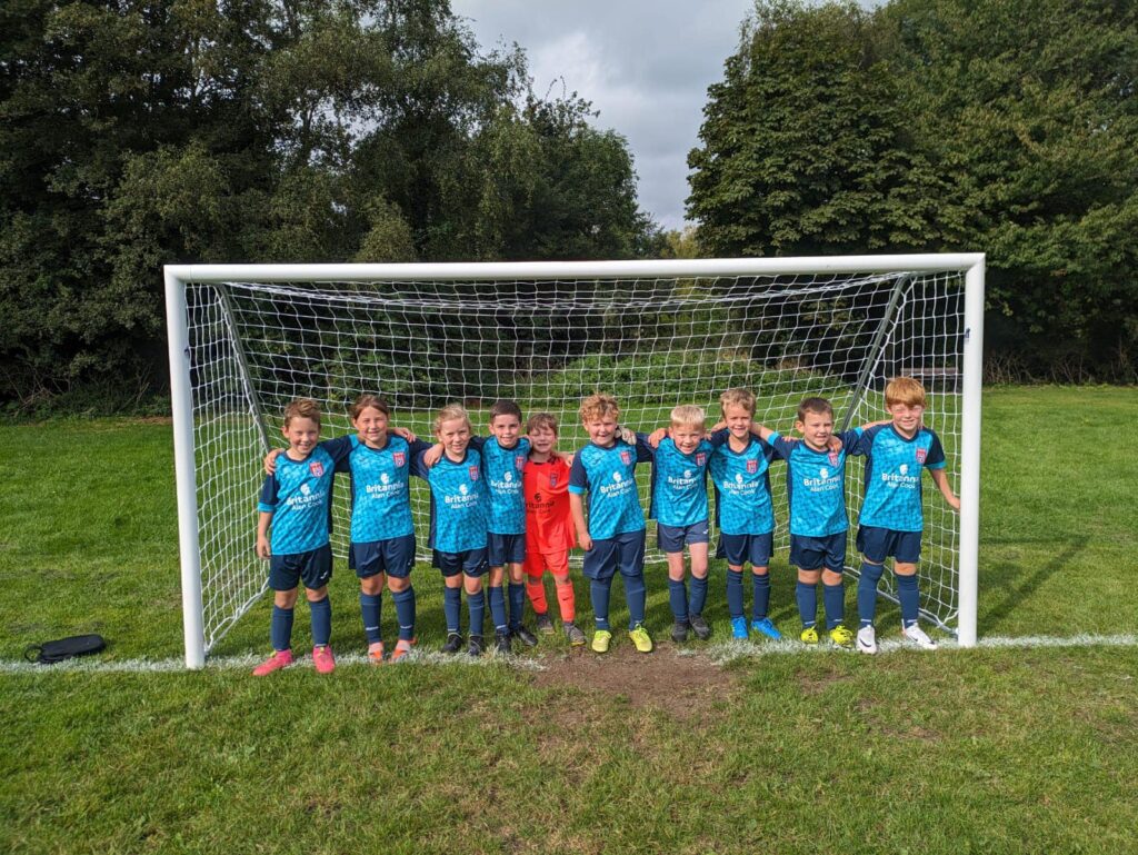 Photo of a football team of children aged around 8 years old all standing in a row on the goal line